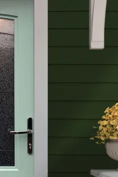 درب ورودی آبی آبی را روی یک خانه سبز جنگلی با تزئینات سفید و گلهای زرد قرار دهید